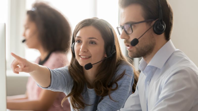 Frau und Mann mit Headsets vor Bildschirm