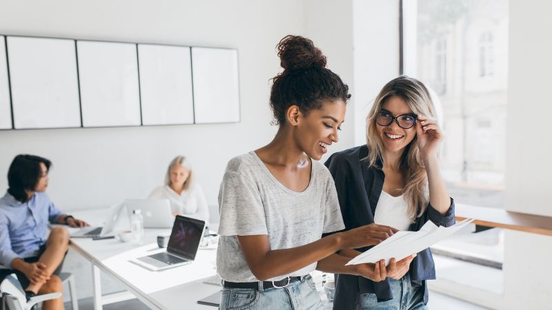 Zwei Frauen im Gespräch und im Hintergrund zwei Frauen an Tisch sitzend