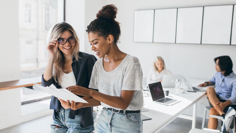 Zwei Frauen im Gespräch und im Hintergrund zwei Frauen an Tisch sitzend