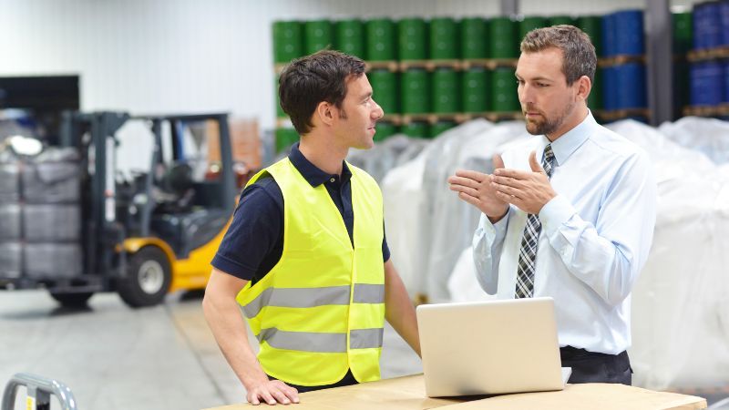 Büroangestellter und Arbeiter mit Laptop in einem Lager