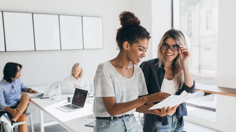 Zwei Frauen im Gespräch und im Hintergrund zwei Frauen an Tisch sitzend